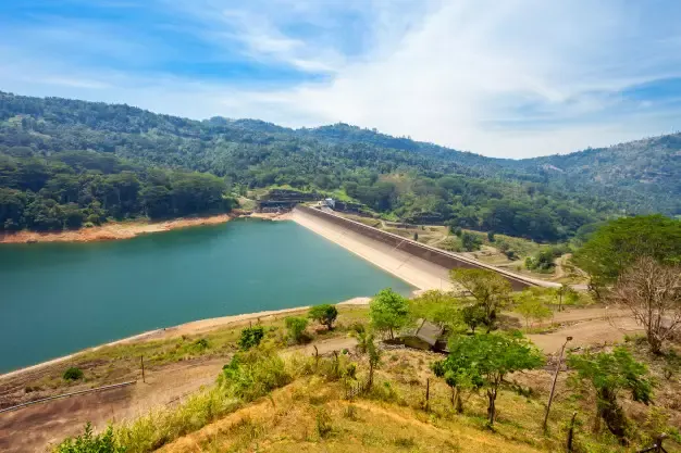 Represa de abastecimento de água com barragem cercada por morros com vegetação