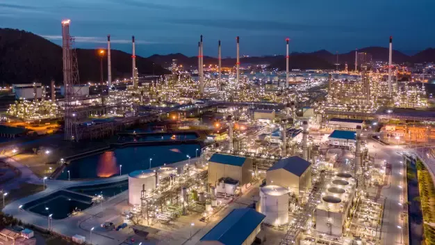 Vista aérea noturna de complexo petroquímico iluminado com tanques e chaminés